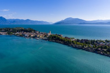 Sirmione yarımadasının açık yaz ışığı altında turkuaz su ve uzak Alpler ile çevrili Garda Gölü 'ne uzanan hava manzarası..