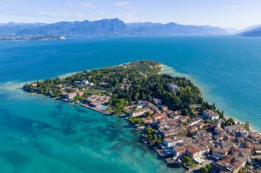 Garda Gölü 'ne çıkan Sirmione Yarımadası' nın havadan görünüşü, yoğun ortaçağ kasabası ve turkuaz su ve alp zeminiyle çevrili göl kenarındaki villalar..