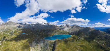 Lago Goillet rezervuarının yüksek irtifa panoraması ve yaz bulutlarının altındaki İtalyan Alpleri kayalık tepeler, çimen yamaçları ve turkuaz su gösteriyor..