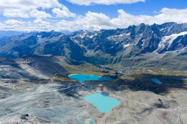 Aosta Vadisi Alplerindeki Valtournenche 'deki Lago Goillet rezervuarının yüksek açılı görüntüsü, turkuaz su, kayalık ön plan ve karlı tepeler.
