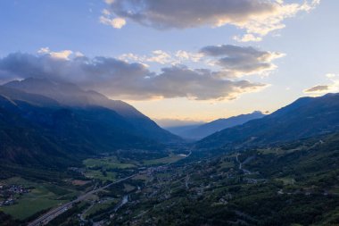 İtalya, Saint-Denis yakınlarındaki Aosta Vadisi 'nin geniş manzarası alp yamaçlarını, köyleri ve parlak yaz günbatımı gökyüzünün altındaki katmanlı dağları gösteriyor..