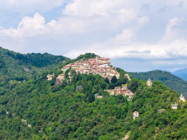 Kuzey İtalya 'da Varese yakınlarındaki Prealpin yamaçlarında sık ormanlarla çevrili kompakt bir tepe köyünün hava manzarası..