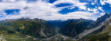 Dolambaçlı otoyolu, ormanlık yamaçları, kayalık tepeleri ve dağınık yaz bulutlarıyla geniş bir dağ vadisi manzarası..