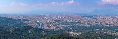 Po Nehri 'ni, yoğun şehir kumaşını ve sisli bir yaz gününde çevreleyen yeşil tepeleri gösteren geniş bir Torino manzarası..
