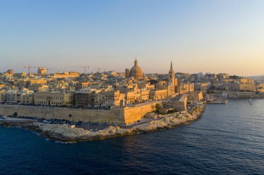 Valletta yarımadasının hava günbatımı manzarası, kireçtaşı kale duvarları, Barok kubbeleri ve Malta 'daki Grand Harbour kıyı şeridi üzerindeki kuleleri gösteriyor..