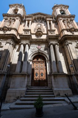 Valletta 'daki Batık Kilise cephesinden Aziz Paul' ün düşük açılı görüntüsü, ikiz çan kuleleri, Barok taş işçiliği, sütunlar ve parlak güneş altında süslü ahşap bir kapı..