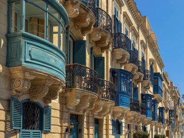 Geleneksel Malta kereste gallarija balkonları ve Valletta 'daki kireçtaşı konaklarına işlenmiş demir korkuluklar. Yaz güneşiyle aydınlatılıyor..
