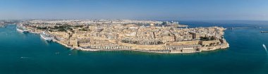 Havadan Valletta yarımadasının kireçtaşı kale duvarları, Grand Harbour rıhtımı, yolcu gemileri ve açık yaz gökyüzü altında Akdeniz manzarası.