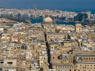 Valletta, Malta üzerindeki hava manzarasında yoğun kireçtaşı binalar, düz çatılar, kilise kubbeleri ve parlak yaz ışığı altında dar sokaklar görülüyor..
