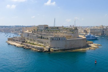 Malta, Birgu rıhtımındaki Fort St Angelo manzarası. Mavi liman ve marina teknelerinin üstündeki taş kaleler gün ışığı altında..