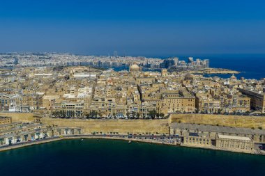 Vallettas kireçtaşı tahkimatı ve Büyük Liman boyunca uzanan yoğun tarihi şehir silueti, Akdeniz ve açık mavi gökyüzü..