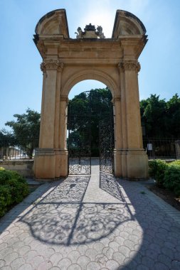 Demirden kapıları olan taş kemer girişi Malta Valletta 'daki Kral V. George eğlence sahalarında gölgeler oluşturuyor..