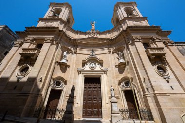 Valletta 'daki St. Dominic Kilisesi' nin alçak açılı görüntüsü kireçtaşı barok cephesini, ikiz çan kulelerini, heykelleri ve açık mavi gökyüzünün altındaki kemerli girişi gösteriyor..