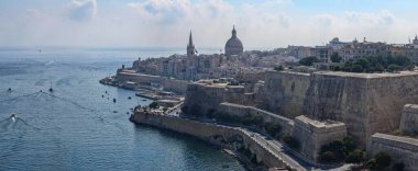 Valletta, Malta 'daki Triton Çeşmesi' nin geniş görüşü, üç bronz triton, bir havza, su jetleri ve asfalt şehir meydanında açık mavi bir gökyüzü tutuyor..