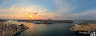 Valletta ve güçlendirilmiş üç şehrin kıyı şeridi, yolcu gemisi ve sakin Akdeniz suyuyla Maltas Grand Harbour üzerindeki hava günbatımı manzarası.