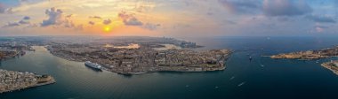 Valletta Yarımadası 'nın ve Maltas Grand Harbour' un geniş hava manzaralı gezgin gemisi, dalgalar ve pastel bir günbatımı gökyüzü altında tekneleri..