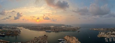 Gün batımında Valletta ve Grand Harbour 'un panoramik havası, yolcu gemisi, kargo gemileri, marinalar ve liman boyunca tarihi kireçtaşı tahkimatları.