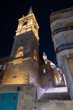 Aydınlatılmış çan kulesi ve Valletta, Malta 'daki St. Paul Katedrali' nin kubbesi geceleri taş basamaklı dar bir sokaktan görülüyor..