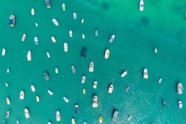 Marsaxlokk marinası, Malta 'da açık turkuaz suya demirlemiş küçük teknelerin yukarıdan aşağı hava görüntüsü, dağınık demirleme noktaları ve dalgalı deniz yüzeyi..