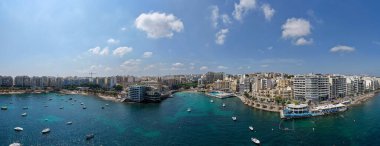 Balluta Körfezi 'nin geniş panoramik manzarası turkuaz Akdeniz suyu, demirli tekneler, deniz kenarı gezinti güvertesi ve yoğun modern apartman dairesi mavi gökyüzünün altında..