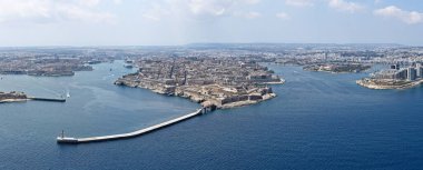 Vallettas İHA panorama güçlendirilmiş yarımada ve Grand Harbour girişi, dalgakıran, yolcu gemisi ve yoğun kireçtaşı şehir blokları yaz bulutları altında.