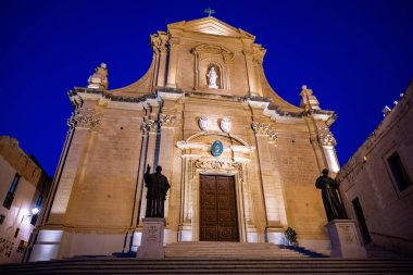 Victoria, Gozo 'daki Aziz George Bazilikası' nın süslü taş portalı ve bronz kapılarına yakın çekim, destek panelleri ve kemerin üzerinde bir ibikli var..