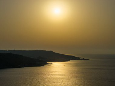 Altın gün batımı Nadur yakınlarındaki Ramla Körfezi açıklarındaki Akdeniz 'e yansıyor. Burun silueti ve durgun suyla..