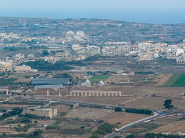 Kercem, Malta yakınlarındaki Gozo Aqueduct harabelerinin uzak bir görüntüsü. Arka planda kuru bir vadiyi geçen taş kemerler ve Xewkija kasabası var..