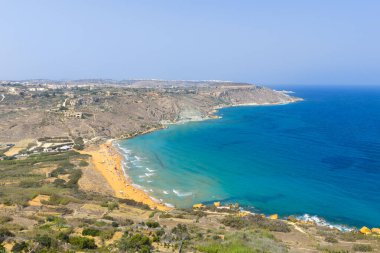 Nadur, Gozo yakınlarındaki Ramla Körfezi sahilinin yüksek kıyı manzarası, kumlu sahil, turkuaz Akdeniz suyu ve kıyı tepeleri üzerindeki yaz sisi..