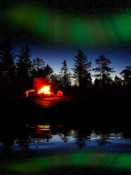 Fire burning at night in a forest with northern lights — Stock Photo, Image