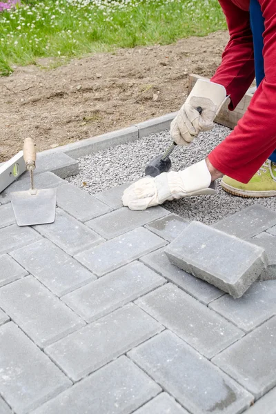 Bricklayer places concrete paving stone blocks for building up a patio, using hammer and spirit level — Stock Photo, Image