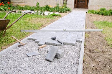 Duvarcı ustası bir veranda kadar bina için beton kaldırım taşı taşları çekiç ve ruh düzeyi kullanarak yerleştirir