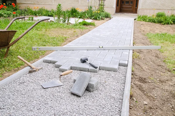 Duvarcı ustası bir veranda kadar bina için beton kaldırım taşı taşları çekiç ve ruh düzeyi kullanarak yerleştirir