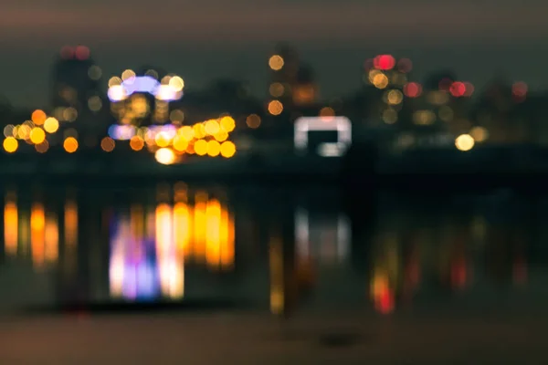 Noite bokeh luz no grande cidade vista com o seu reflexo no rio água, abstrato desfocado borrão fundo — Fotografia de Stock