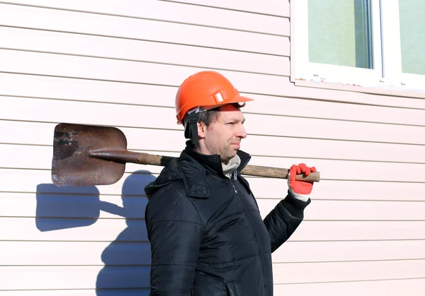 A munkavállaló a narancssárga kemény kalap lapáttal a kezében — Stock Fotó