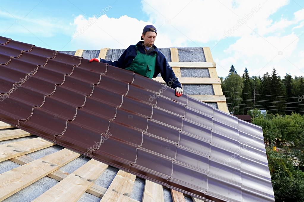 Worker puts the metal tiles on the roof 