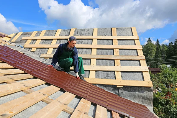 Lavoratore mette le piastrelle metalliche sul tetto di una casa di legno — Foto Stock