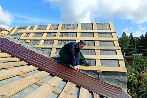 Travailleur met les tuiles métalliques sur le toit d'une maison en bois — Photo