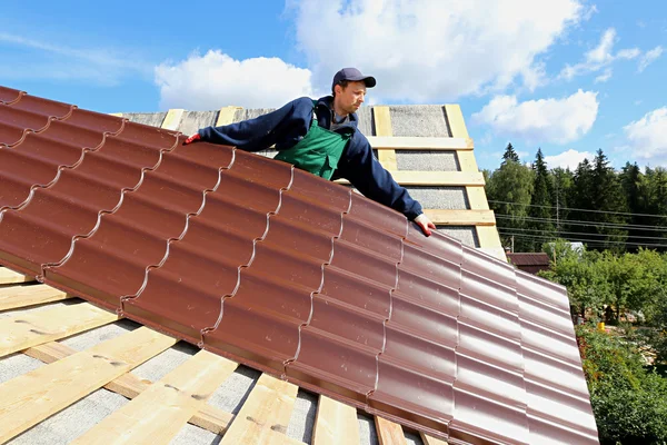 Worker puts the metal tiles on the roof of a wooden house — Stock Photo, Image