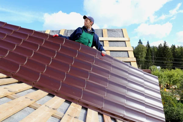 Travailleur met les tuiles métalliques sur le toit d'une maison en bois — Photo