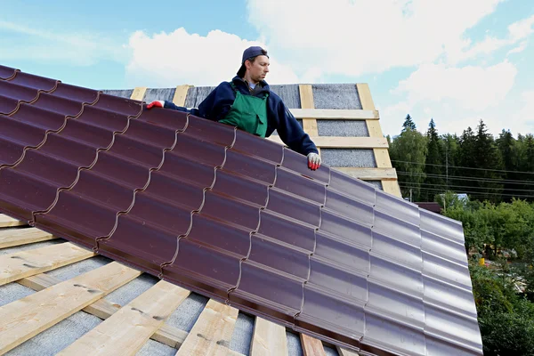Рабочий кладет металлическую плитку на крышу деревянного дома — стоковое фото