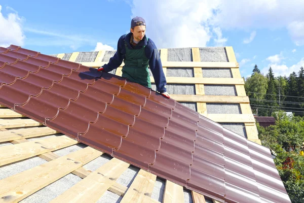 Werknemer legt de metalen tegels op het dak van een houten huis Stockfoto