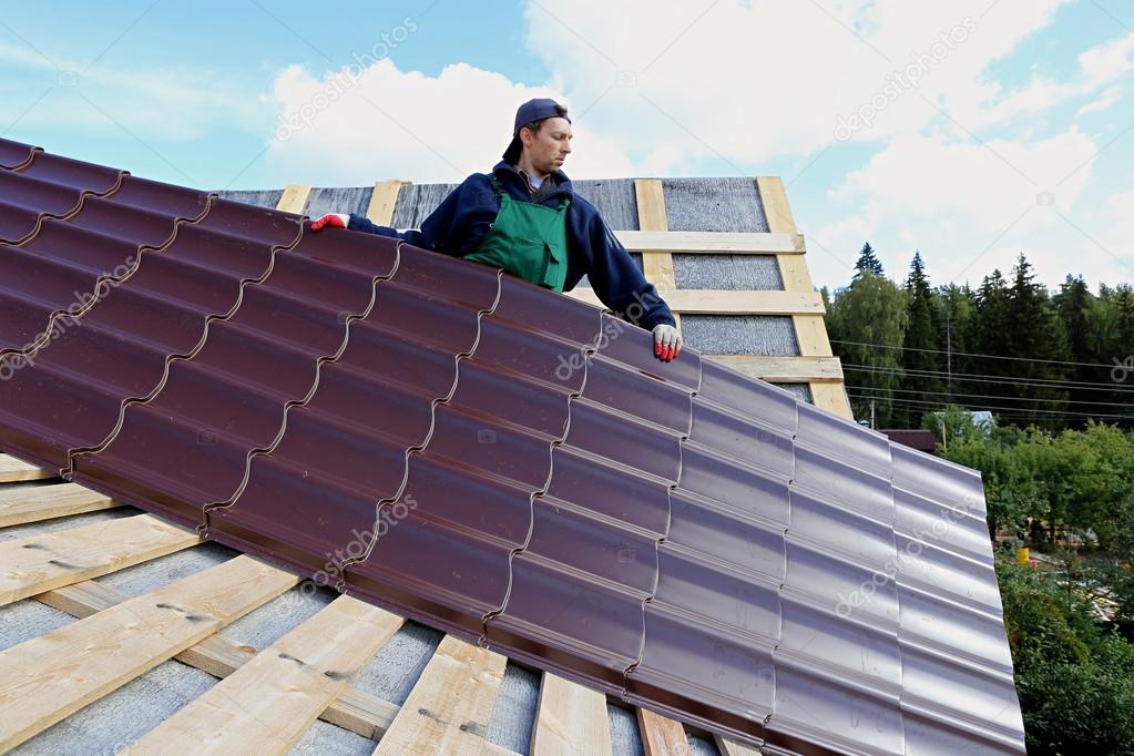 Worker puts the metal tiles on the roof of a wooden house