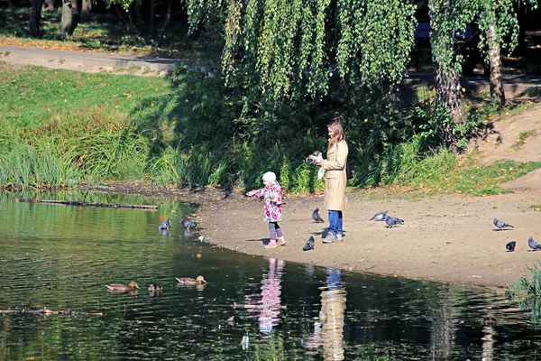 Menina com sua mãe alimentar pássaros na lagoa — Fotografia de Stock