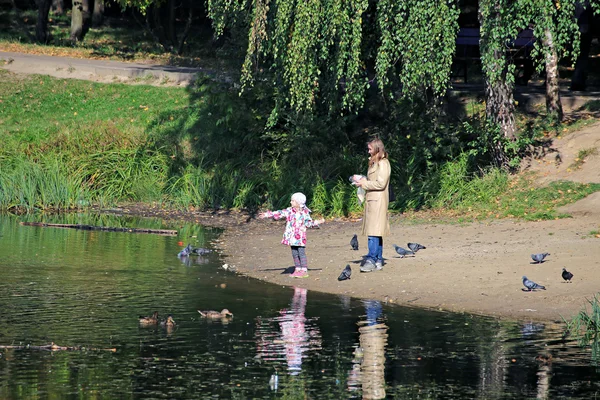 Menina com sua mãe alimentar pássaros na lagoa — Fotografia de Stock