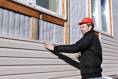 A worker installs panels beige siding on the facade clipart