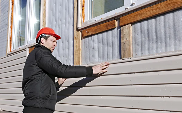 Een werknemer installeert panelen beige siding op de gevel Stockfoto