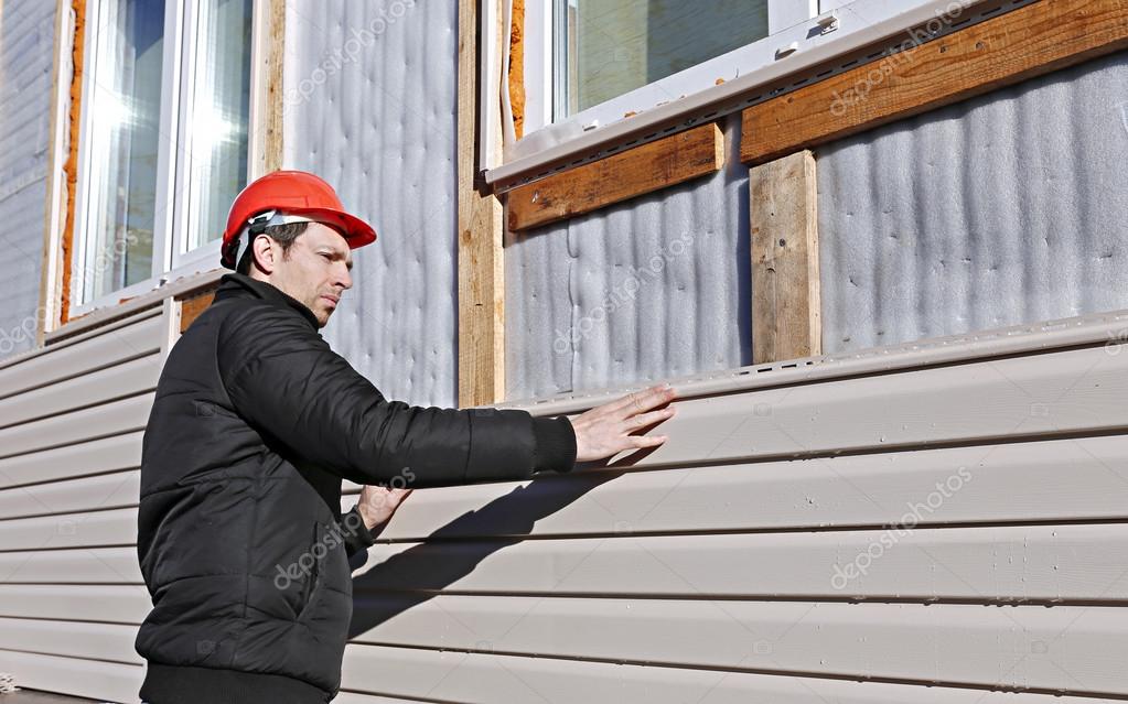 A worker installs panels beige siding on the facade Stock Photo by