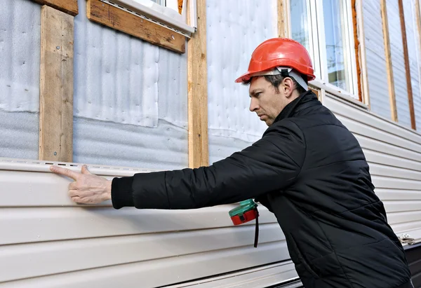 Een arbeider installeert panelen beige gevel op de gevel van het huis Stockafbeelding