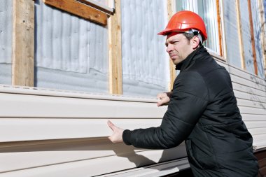 A worker installs panels beige siding on the facade of the house clipart